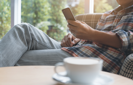 Male relaxing on recliner scrolling through cell phone with coffee cup